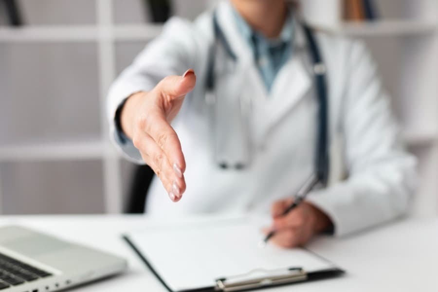 Medico sentado estendendo a mão para cumprimentar Medico sentado estendendo a mão para cumprimentar